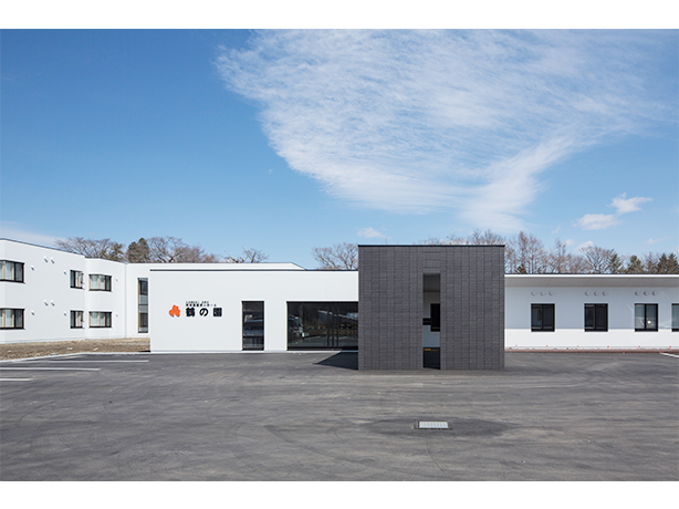 介護施設の建物外観。白と黒のモダンな建築デザイン、広い駐車場。